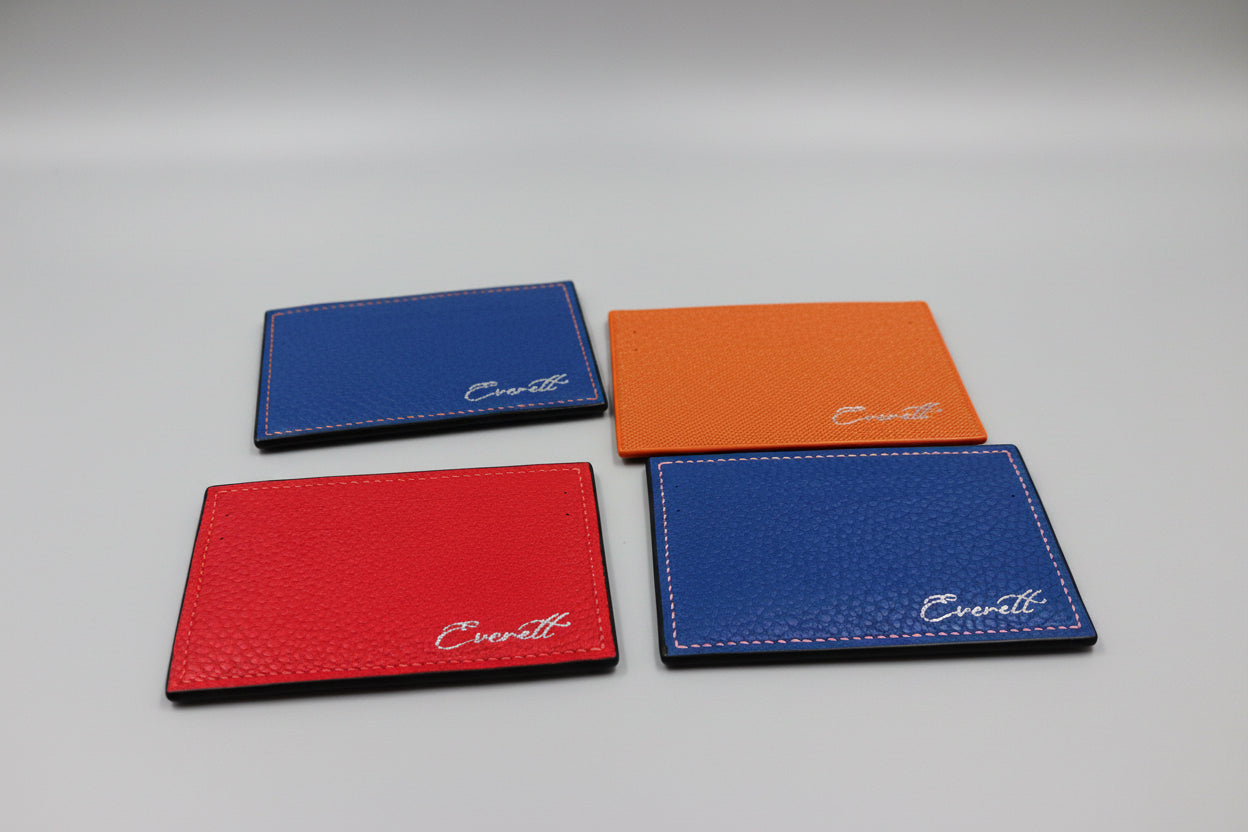 Four leather cardholders in blue, red, and orange on a marble surface with 'Everett' branding.