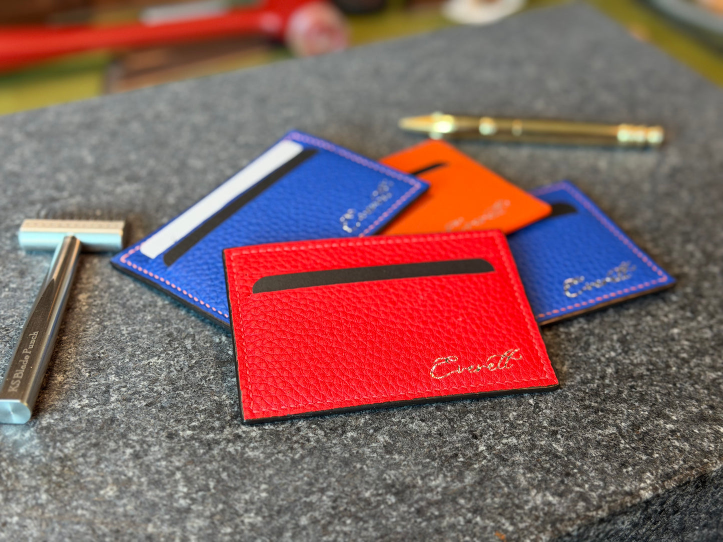 Red, blue, and orange card holders on a textured surface with tools in the background.